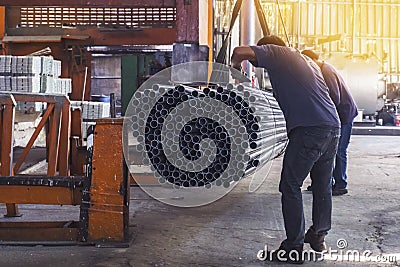 Two workers in uniform using lifting machines to move metal pipe in a sheet metal factory Stock Photo