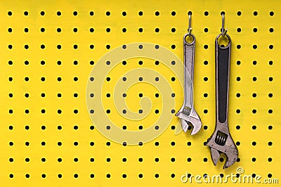 Two wrenches hang from hooks on yellow pegboard Stock Photo