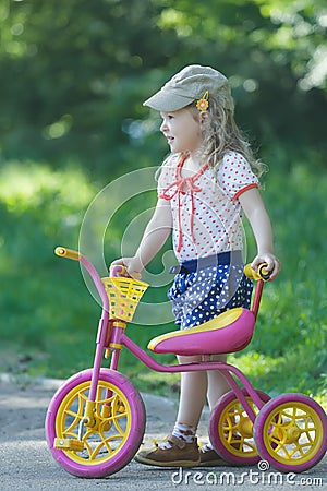 Two year-old standing near pink and yellow kids tricycle with steel frame Stock Photo