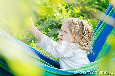 Two year-old toddler girl is laughing and playing in striped blue-green Brazilian hammock Stock Photo