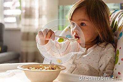 Two years old eats brakefast by herself with a spoon Stock Photo