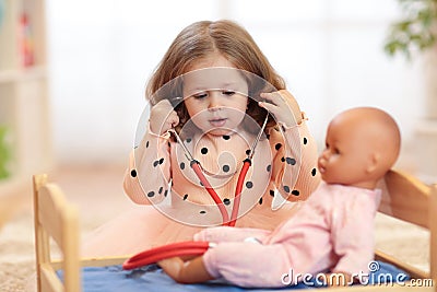 Two years old girl playing doctor with doll in the nursery Stock Photo