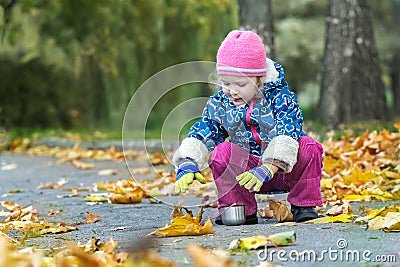 Two years old girl stretching her hand to metal thermos flask cup hunkering at autumn foliage covering backdrop Stock Photo