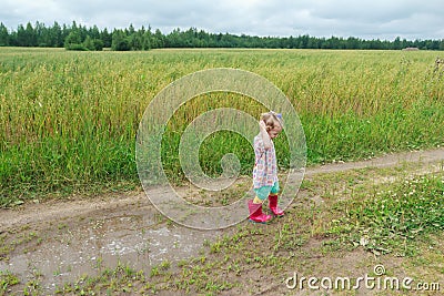 Two years old preschooler girl playing on farm dirt road near puddle Stock Photo
