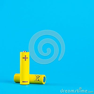 Two yellow AA alkaline batteries or NiMH rechargeable batteries on a blue background with space for text. Power elements Stock Photo