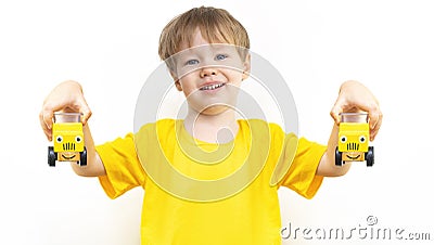 Two yellow cars with painted eyes and smile in hands of Little European happy happy child boy. Kid holds toy cars. Concept of Stock Photo