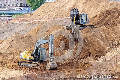 Two yellow crawler excavators on a construction site - one on the lower level, the other on top of a pile of earth Editorial Stock Photo