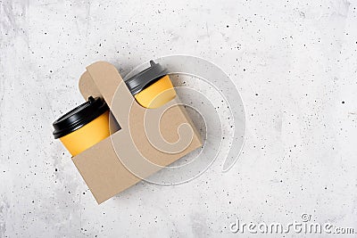 Two yellow paper cups in craft cup holder, light gray concrete background. Top view. Coffee to go. Copy space on the right. Place Stock Photo