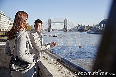Two young adult women standing at the Thames riverside talking, Tower Bridge in the background Stock Photo