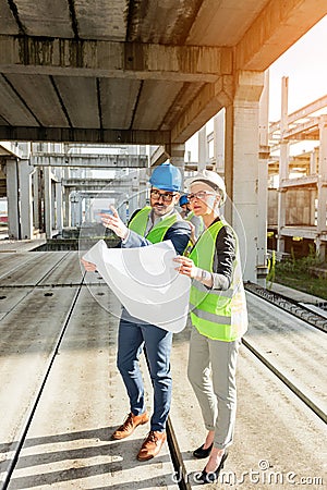 Two young architects visiting large construction site, looking at floor plans Stock Photo