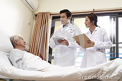 Two young asian doctors talking old man at bedside Stock Photo