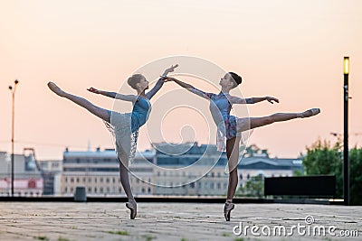 Two young ballerinas dancing in pointe shoes in city against the backdrop of sunset sky Stock Photo