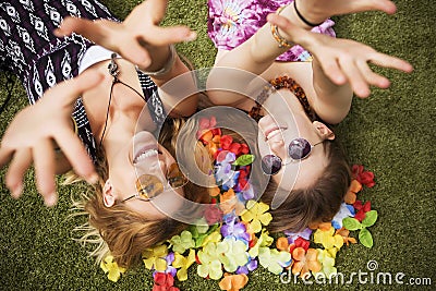 Two young beautiful blonde hipster girls on summer day having fun in european city. Green grass on a background and flower leafs. Stock Photo