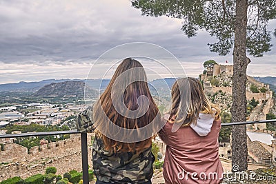 Two young blond-haired and brown-haired teenage girls are observing the landscape inside Xativa castle in Valencia, Spain Editorial Stock Photo