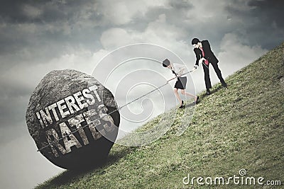 Workers pull a stone with Interest Rates text Stock Photo