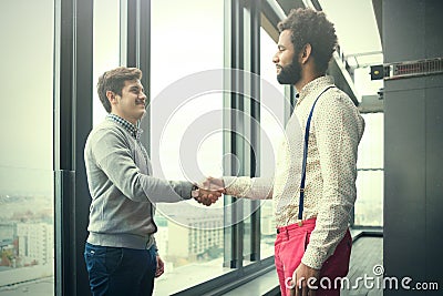 Two young businessmen shaking hands in modern office hall Stock Photo