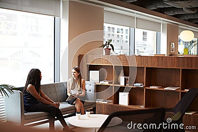 Two Young Businesswomen Having Informal Interview In Cafeteria Area At Graduate Recruitment Assessment Day Stock Photo