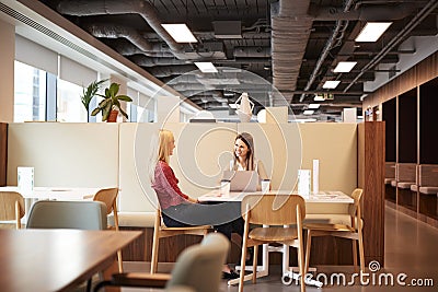 Two Young Businesswomen Having Informal Interview In Cafeteria Area At Graduate Recruitment Assessment Day Stock Photo
