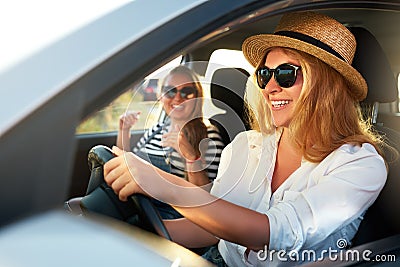 Two young cheerful smiling women in a car on vacation trip to the sea beach. Girl in glasses driving a vehicle from Stock Photo