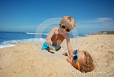 On the beach, two kids in sunglasses enjoy playtime with sand Stock Photo