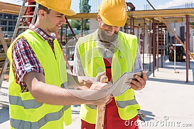 Two young construction workers smiling while using a tablet duri Stock Photo