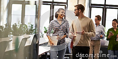 Two young diverse business people, male and female coworkers talking, discussing project and smiling while walking down Stock Photo