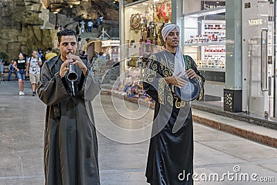 Two young Egyptian men in traditional dress walking along night street , playing folk instruments. Editorial Stock Photo