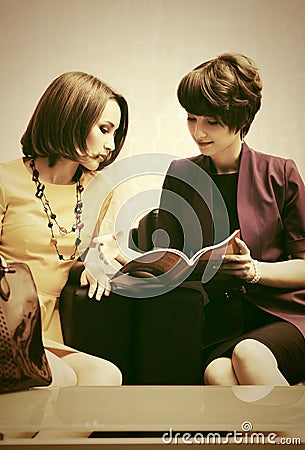 Two young fashion women reading a magazine in showroom Stock Photo