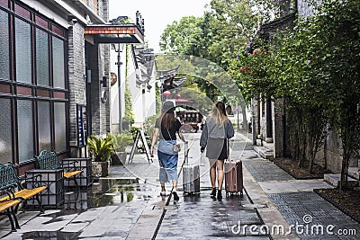 Two young fashionable girls walking with suitcases in the old gate east scenic area Editorial Stock Photo