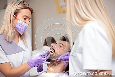 Two young female dentists working in dental clinic. Whitening male patient`s teeth and using tone chart to mach color Stock Photo