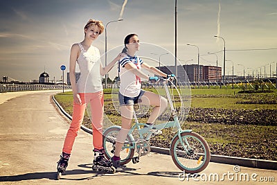 Two young female friends one on a bicycle, one on a roler scates Stock Photo