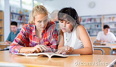 Two young friendly female pupils talking, reading books and making notes Stock Photo