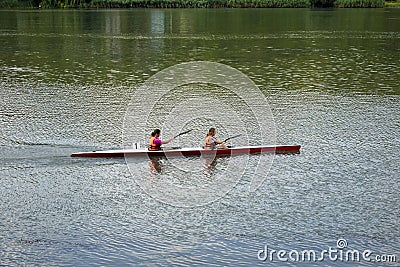 Two young girl athletes in life jackets are sailing canoe on river, controlling oars. Active outdoor sports training. Side view. Editorial Stock Photo