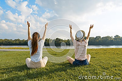 Two young girls meditate in the park near the river, back view, the girls raised their hands up, golden hour Stock Photo