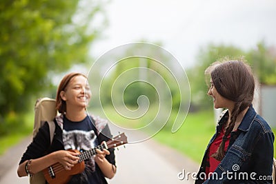 Two young girls walking together, laughing and playing ukulele Stock Photo