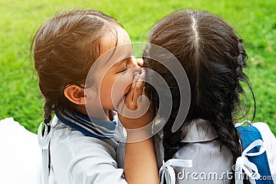 Two young girls whispering and sharing a secret during playground session on green glass background Stock Photo