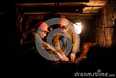 Two young guys in a working uniform and protective helmets, sitting in a low tunnel. Workers of the mine Stock Photo
