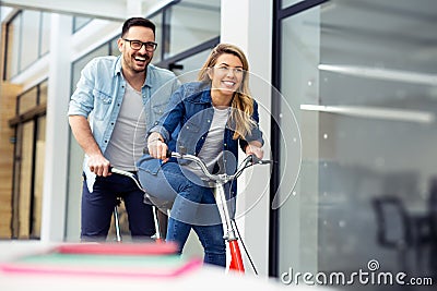 Two happy coworkers riding bicycle in the office together. Making people laugh. Stock Photo