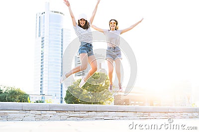 Two young happy hipster girls having fun, smiling, laughing, jumping, walking outdoor on the street, summer relax Stock Photo