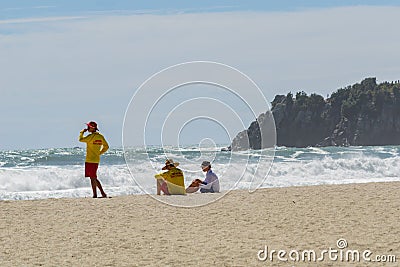 Two young lifeguards and a boy sit on hazy beach watch the rough dangerous surf Editorial Stock Photo