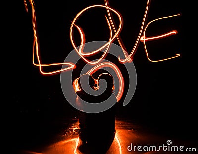 Two young lovers paint a heart on fire. Silhouette of couple and Love words on a dark background Stock Photo