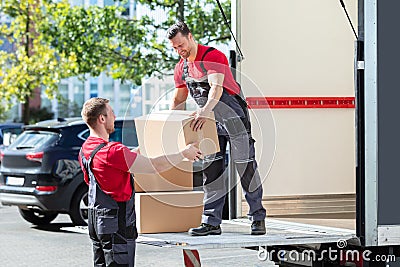 Two Young Male Movers Carrying Cardboard Boxes From Truck Stock Photo