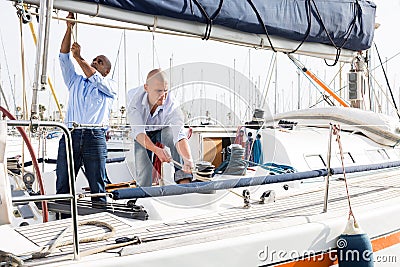 Two men in blue shirts and jeans working on sailing yacht in the port Stock Photo