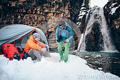 Two young professional male tourists are preparing to camp in the mountains near the river in winter. Stock Photo