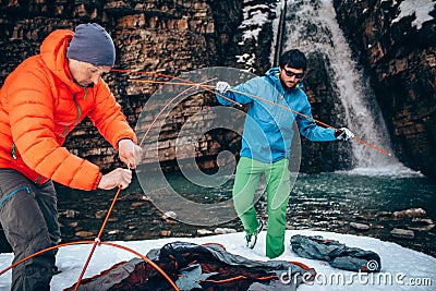 Two young professional male tourists are preparing to camp in the mountains near the river in winter. Stock Photo