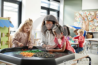 Two young schoolgirls standing at a table playing a game with their female teacher in an infant school classroom, selective focus Stock Photo