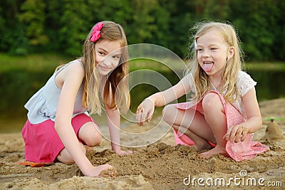 Two young sisters having fun on a sandy lake beach on warm and sunny summer day. Kids playing by the river Stock Photo