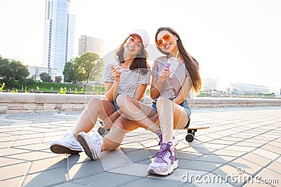 Two Young Woman sitting on Skateboard Happy Smiling. Playful Friends Enjoy Sunny day. Outdoor Urban. Beautiful Model Stock Photo