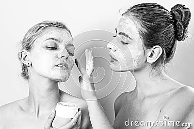 Two young women applying moisturizer cream on their face. Photo of careful friends receiving spa treatments. Home Stock Photo