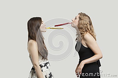 Two young women blowing party puffers while looking at each other against gray background Stock Photo